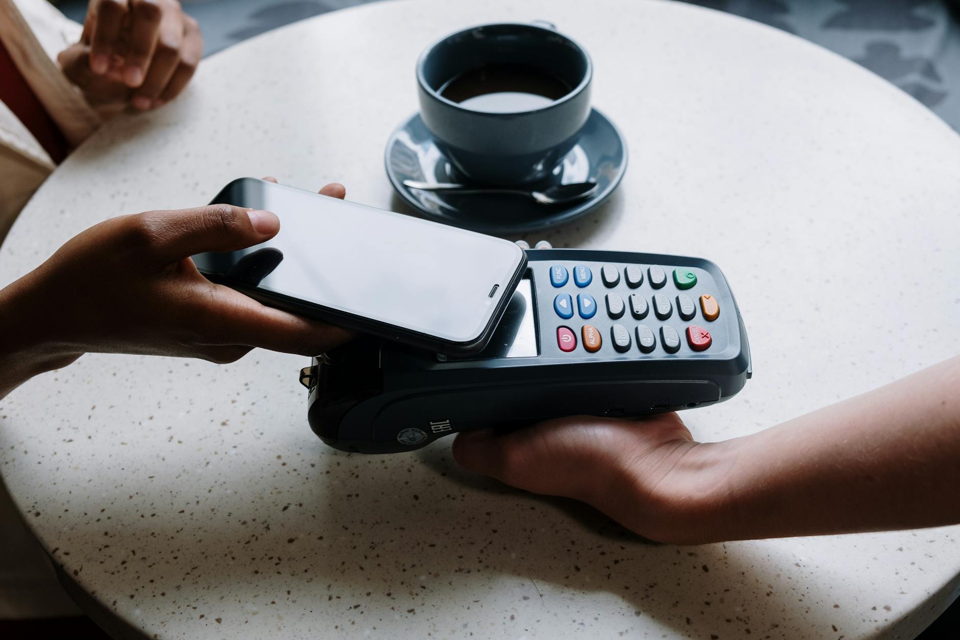 Person using a smartphone for a contactless payment with a card reader on a cafe table — fintech mobile payment