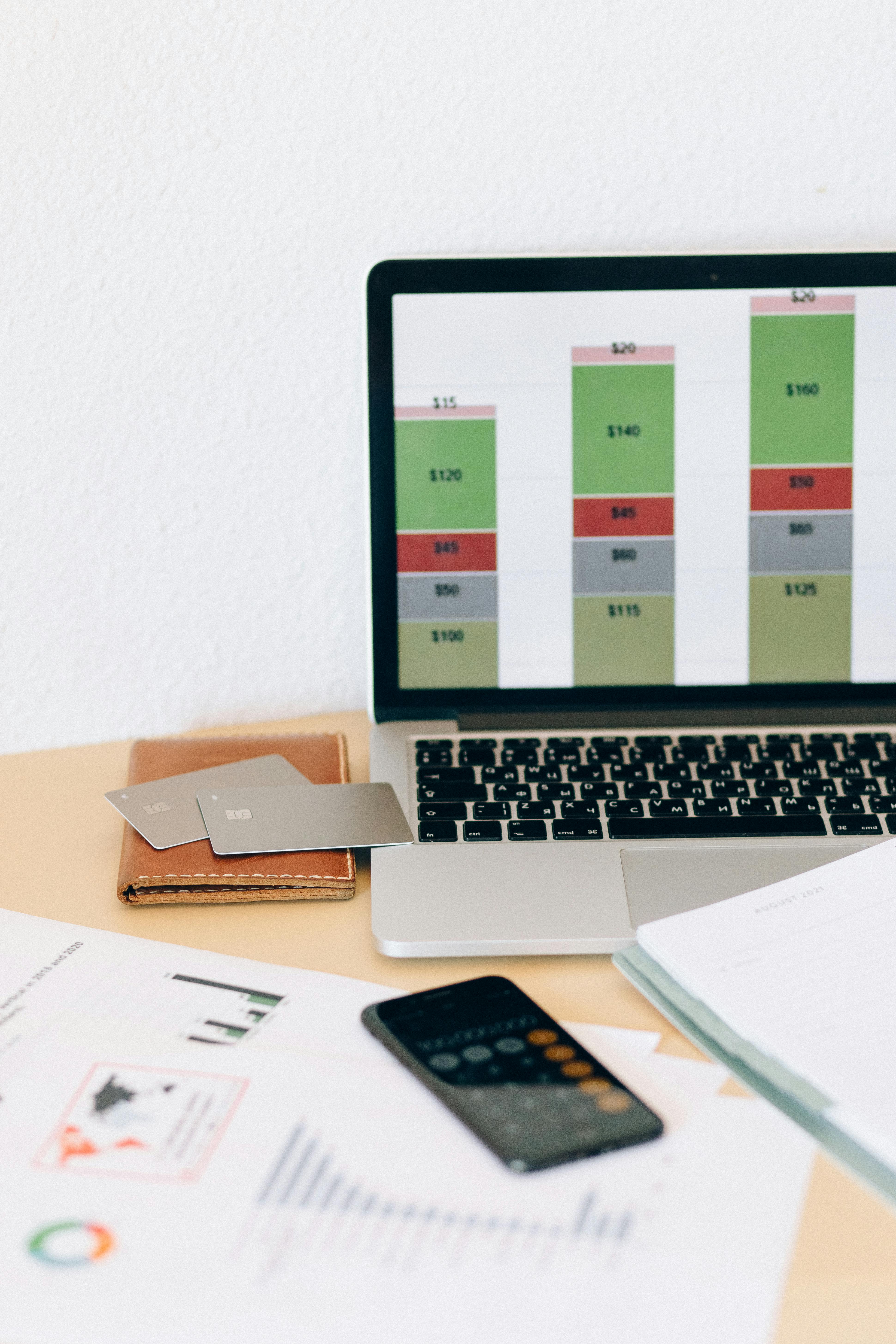 Laptop displaying financial chart alongside documents and credit cards on desk, representing credit scoring and financial analytics