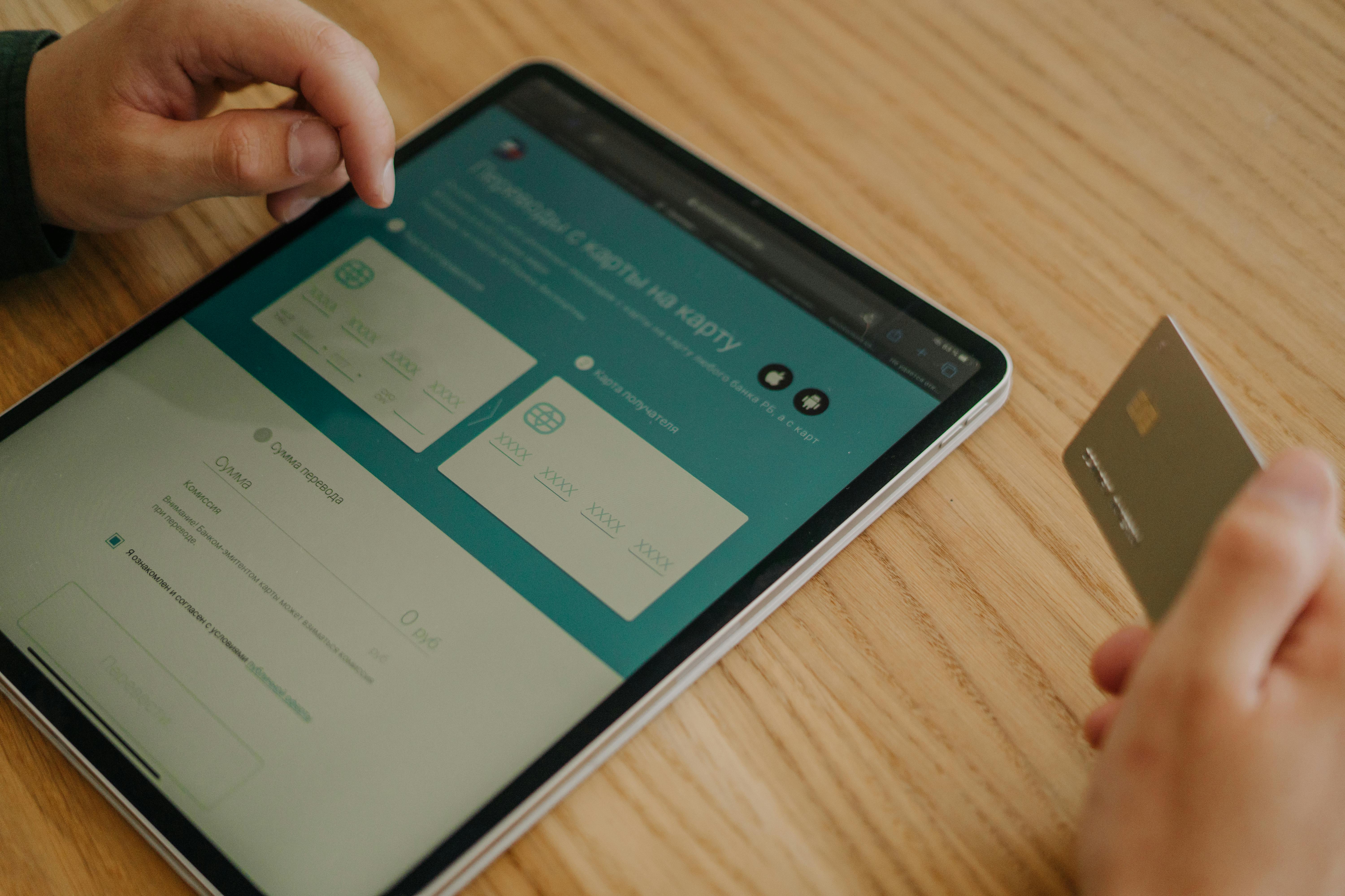 Person making an online purchase using a tablet and credit card on a wooden table