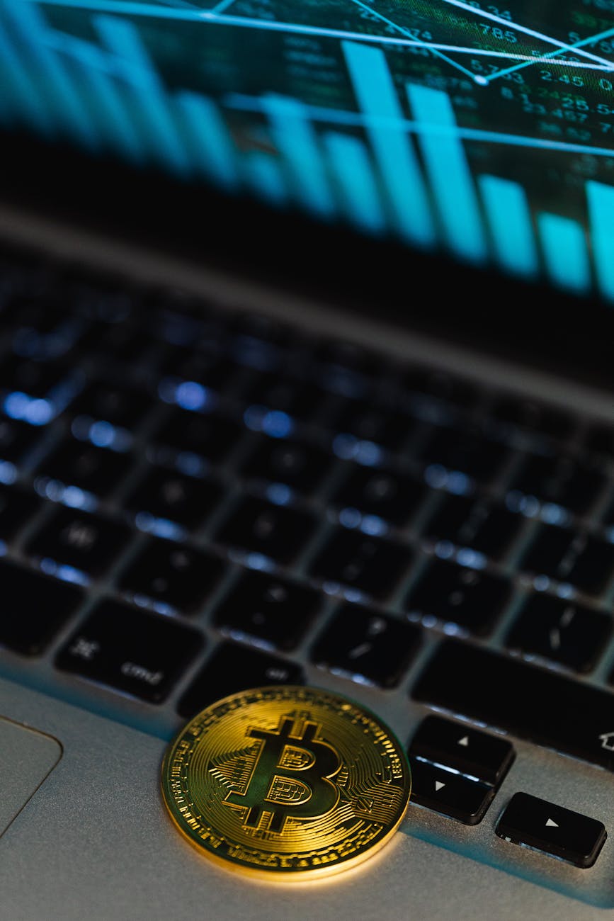 Gold Bitcoin coin lying on a laptop keyboard with a trading chart on the screen.