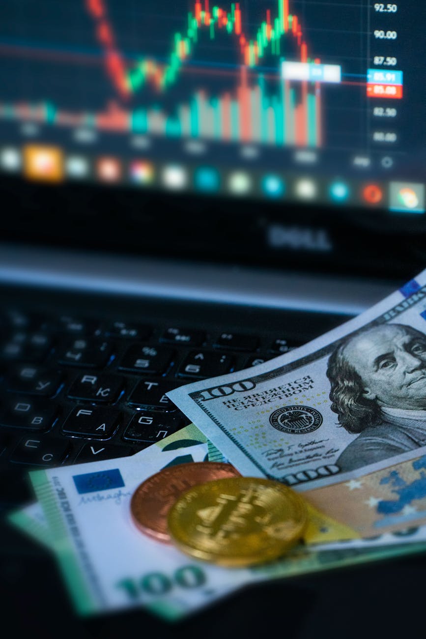 Golden bitcoin coins and banknotes in front of a financial trading chart on a laptop