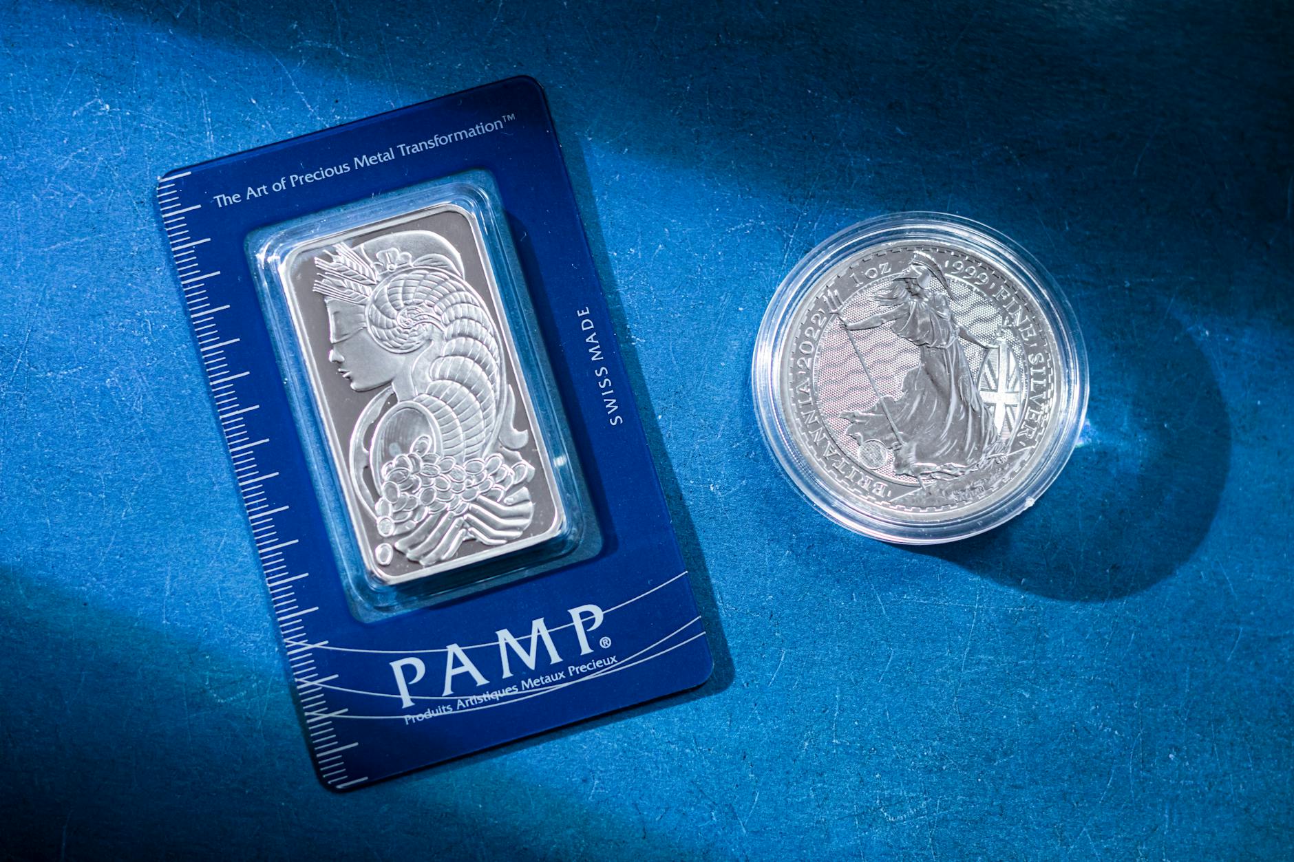 Silver coin and gold PAMP bullion bar on a textured surface