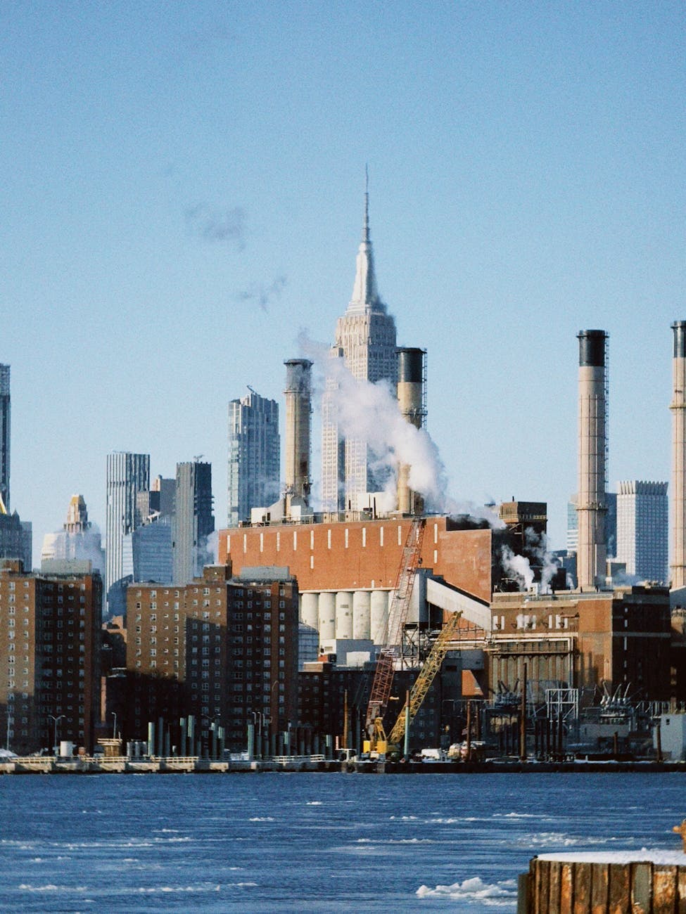 Smoke rises from factories with the iconic New York City skyline in the background.