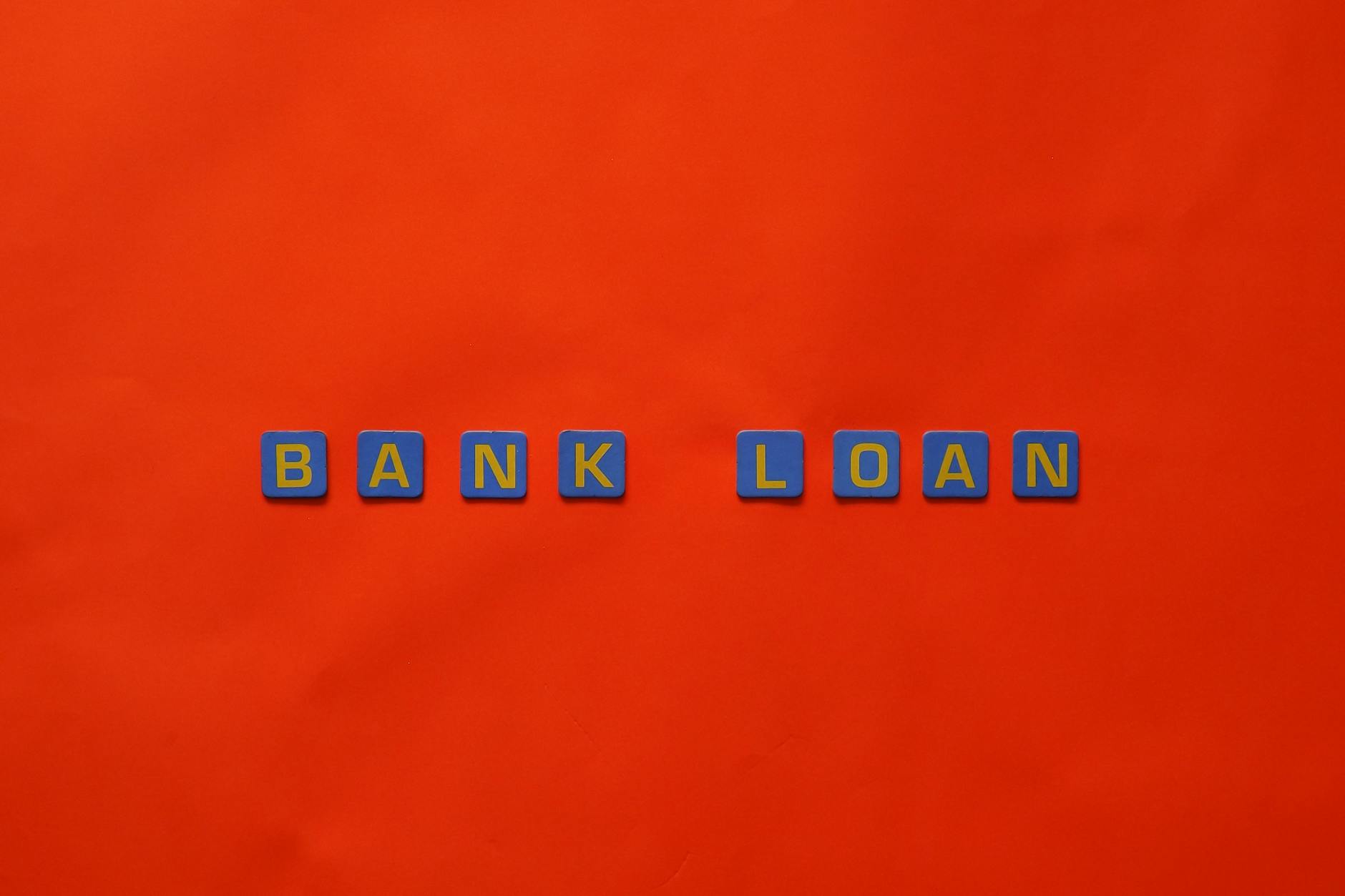 Wooden letters spelling bank loan on a red desk, illustrating credit-market risk and financing conditions.