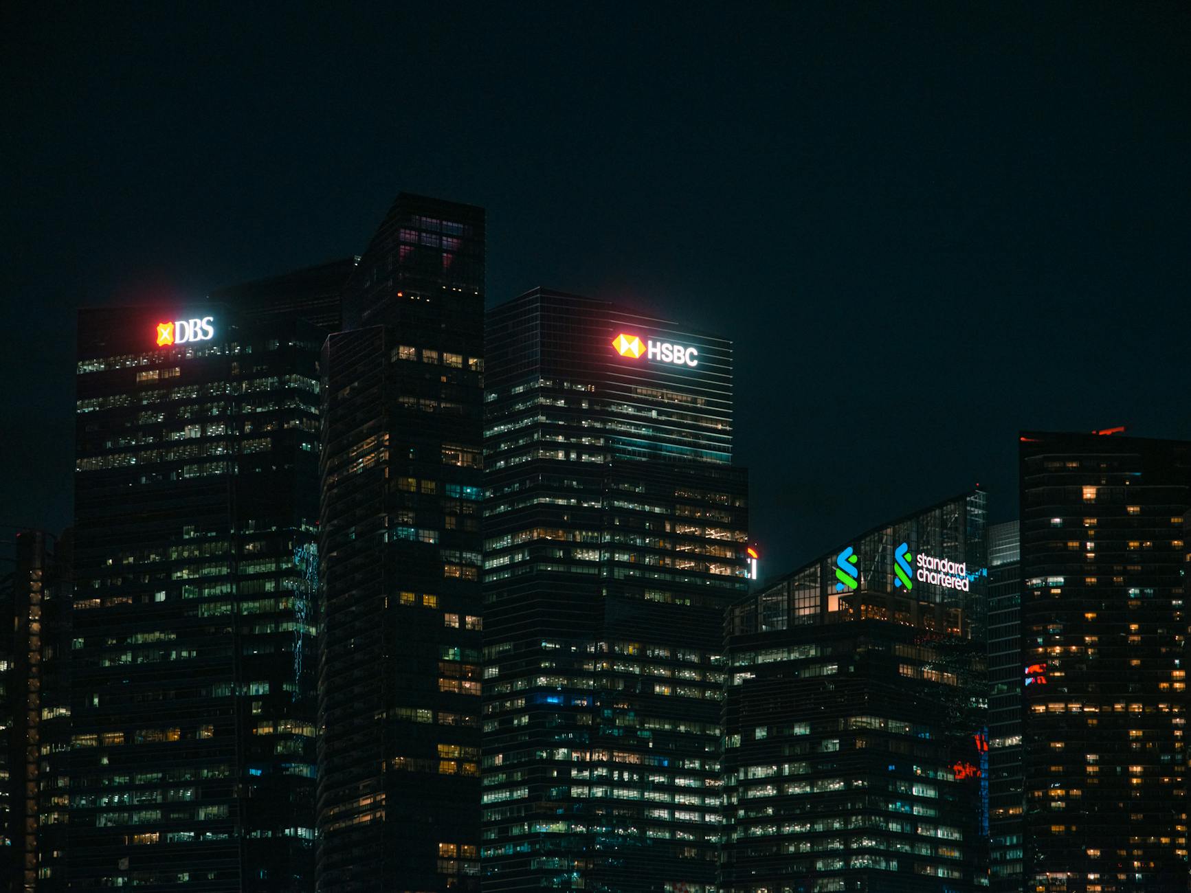 Illuminated city skyscrapers of major banks in Singapore's financial district at night.