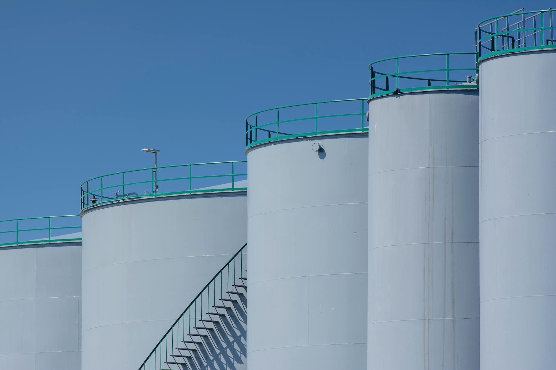 Large industrial storage tanks with green railings against a clear blue sky