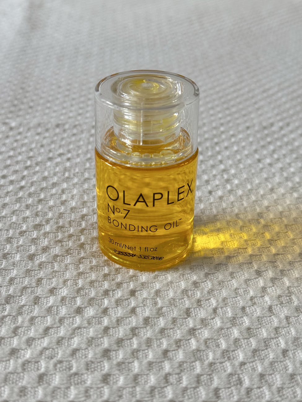Clear bottle of Olaplex No.7 Bonding Oil placed on a white textured surface.