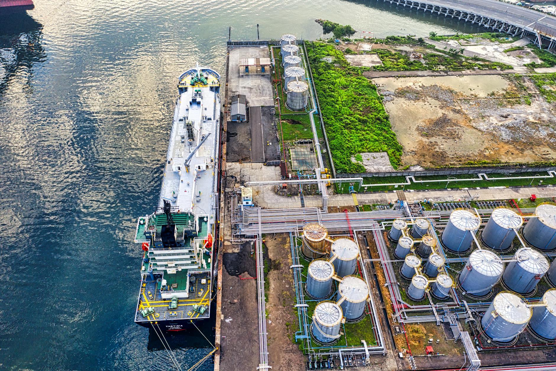 Aerial view of a ship docking at an industrial port with storage tanks, representing petrochemical cargo flows into Asia.