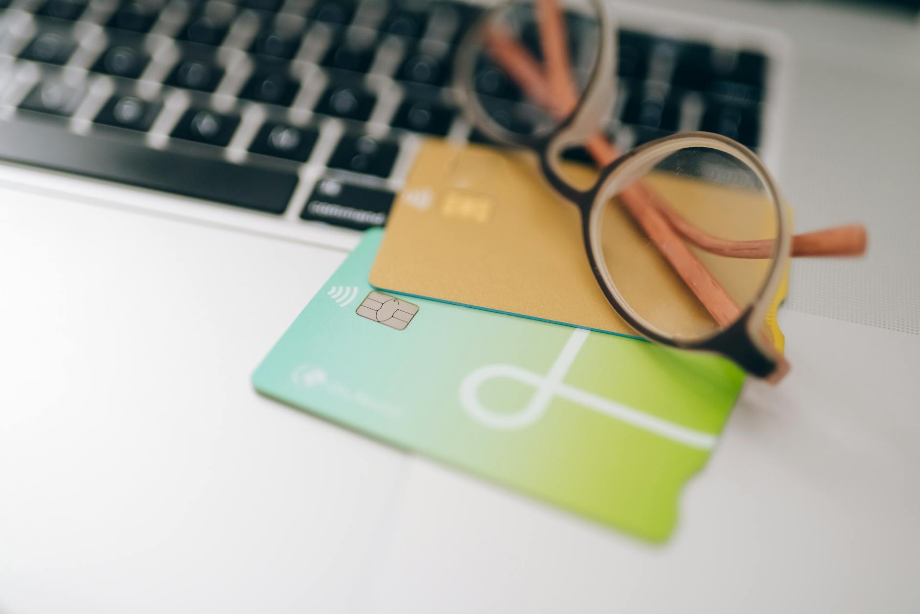 Credit cards and eyeglasses resting on a laptop keyboard, illustrating digital banking and account-linking infrastructure.