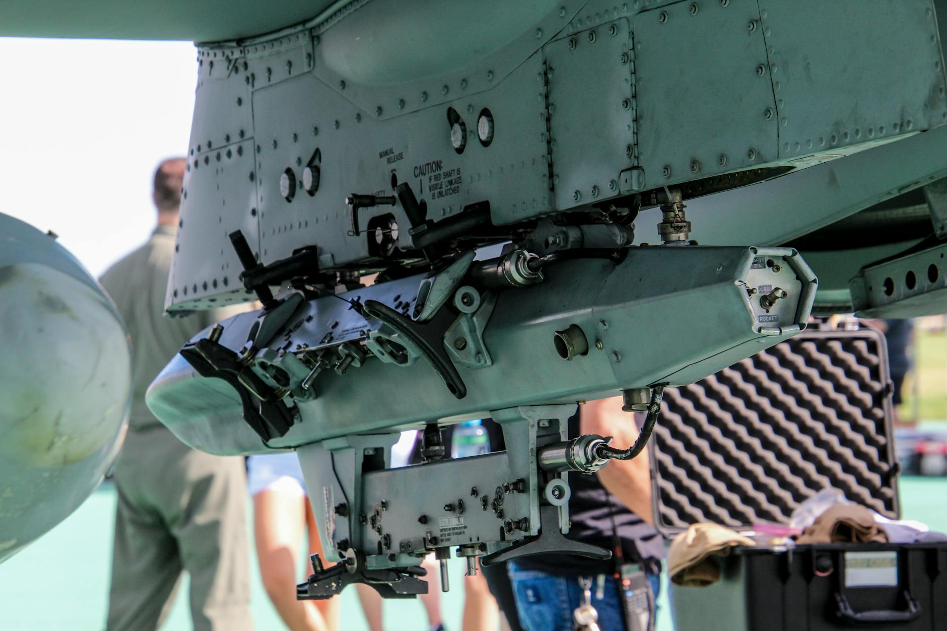 Detailed view of a military aircraft machinery component with people in the background.