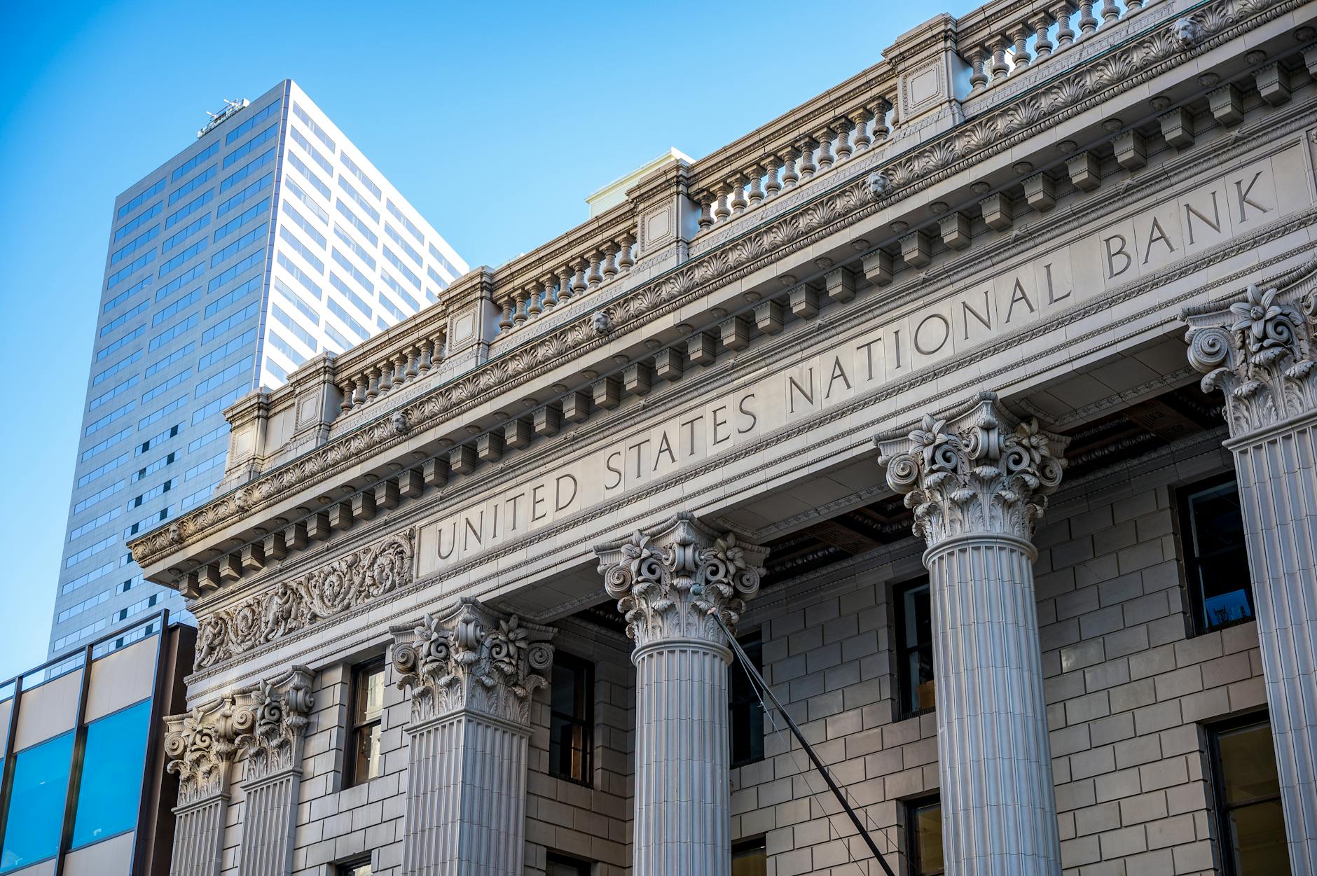 Exterior of a historic national bank with decorative columns and a modern office tower behind it.