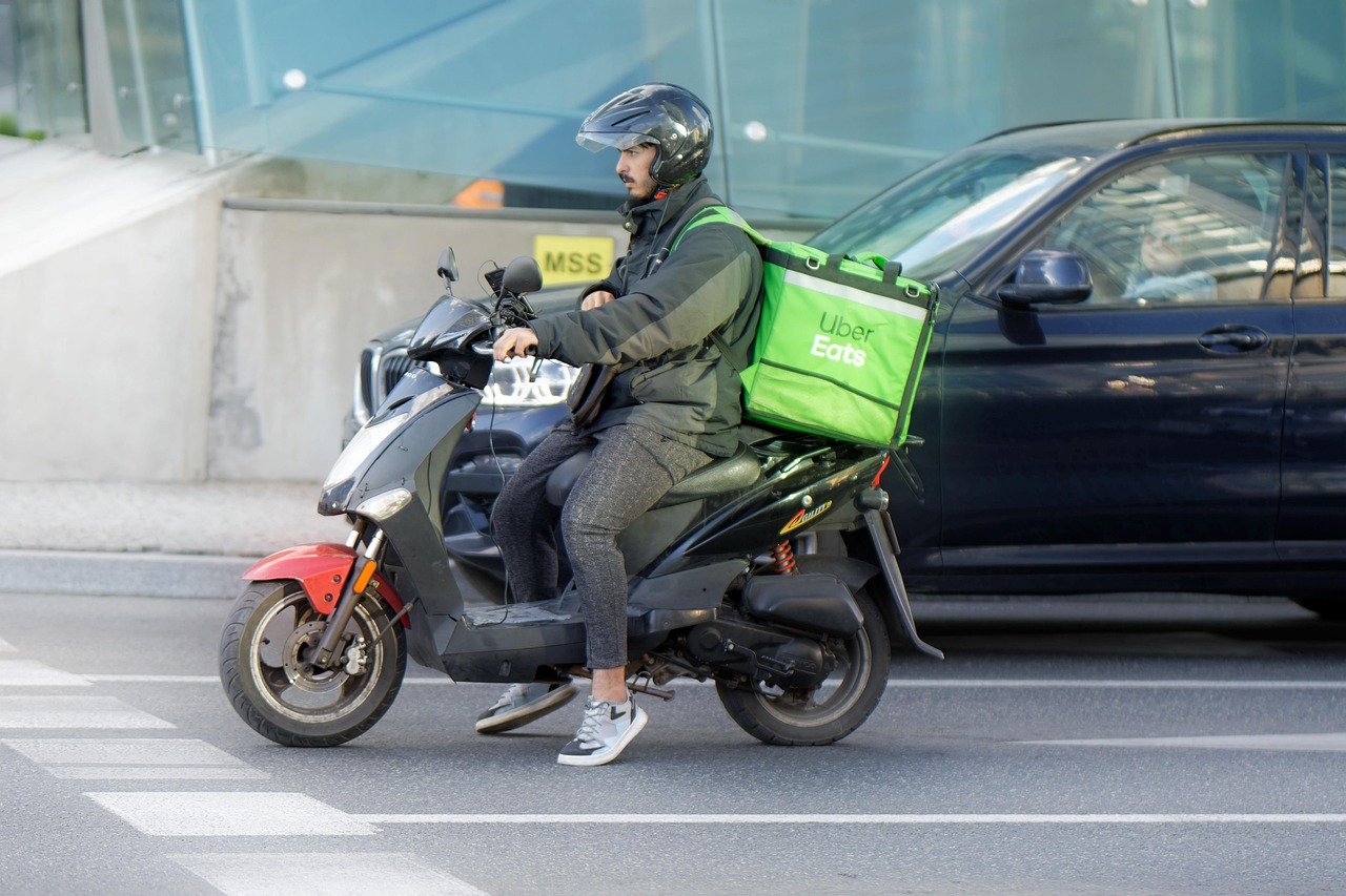Food-delivery courier on a motorcycle waiting in city traffic.