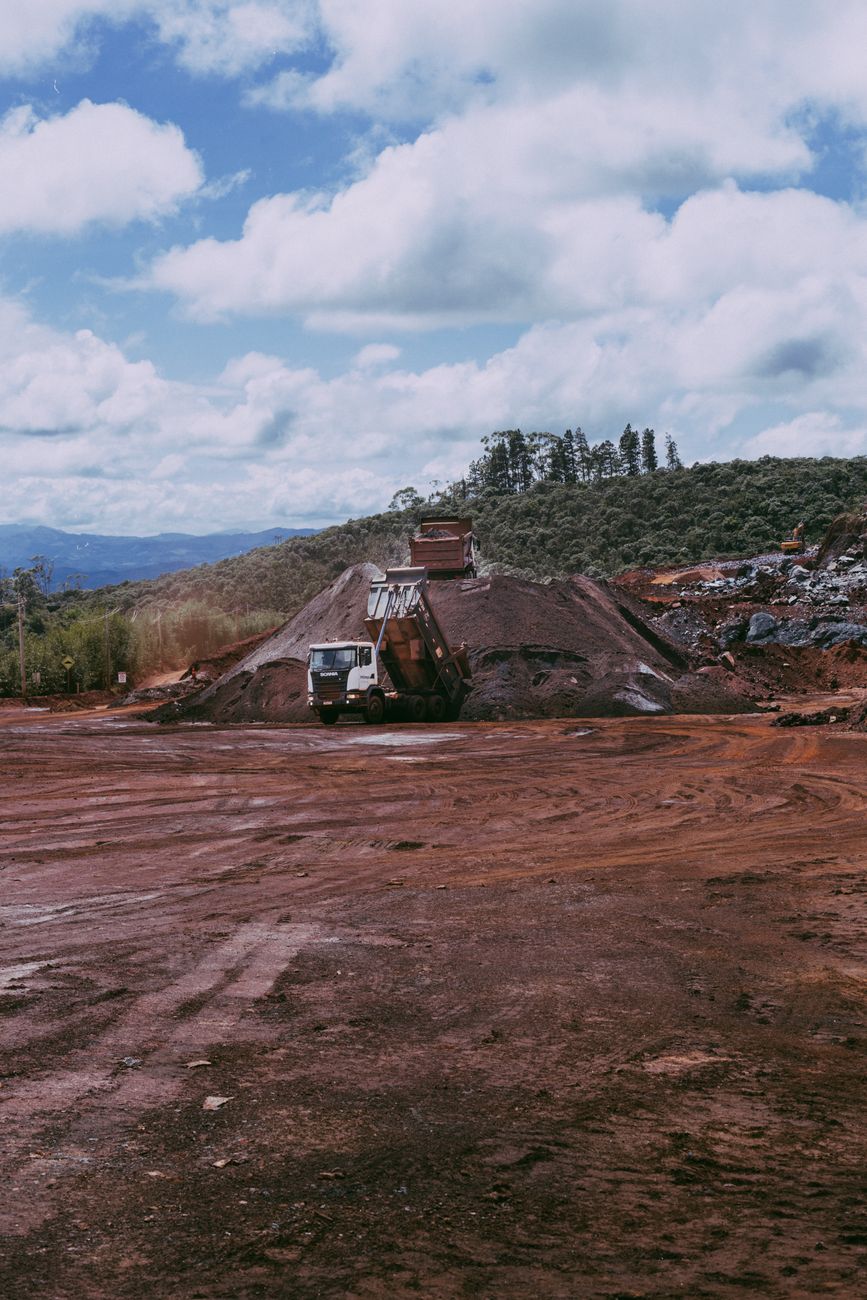 Wide view of a mining site with dump trucks and red dirt under a cloudy sky