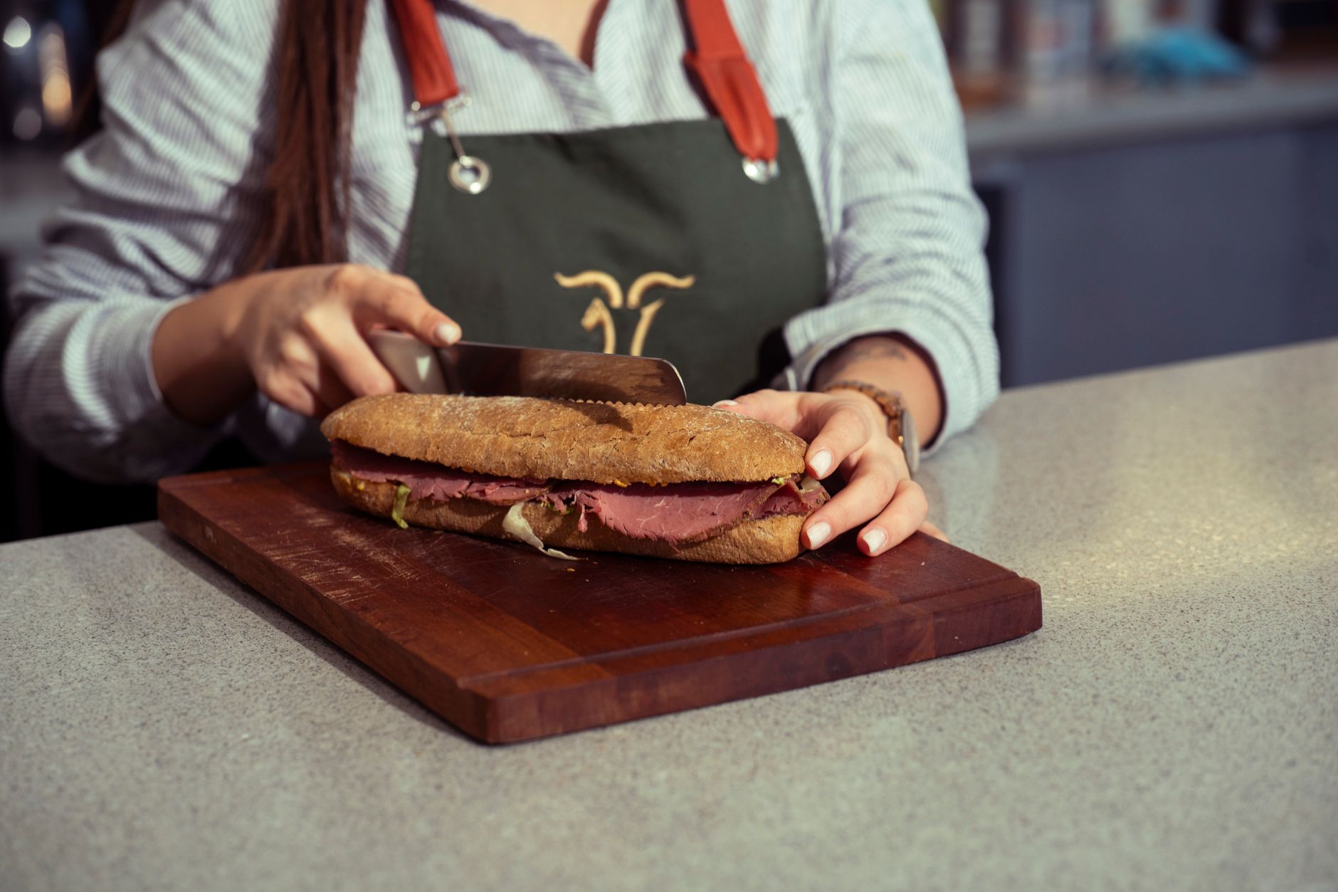Chef slicing a large sandwich on a wooden cutting board