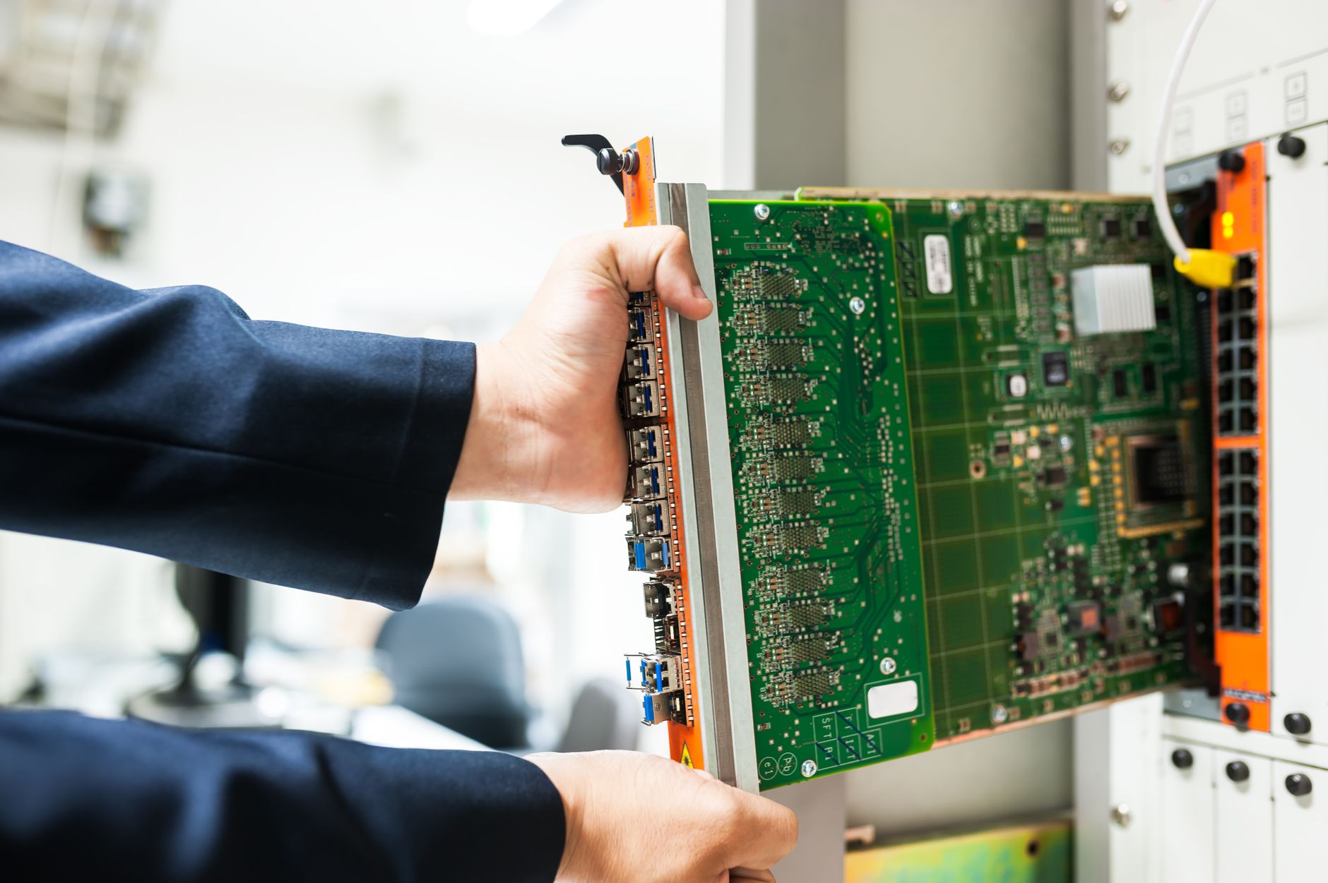 A technician inserts a circuit board into a server rack in a data-centre environment.