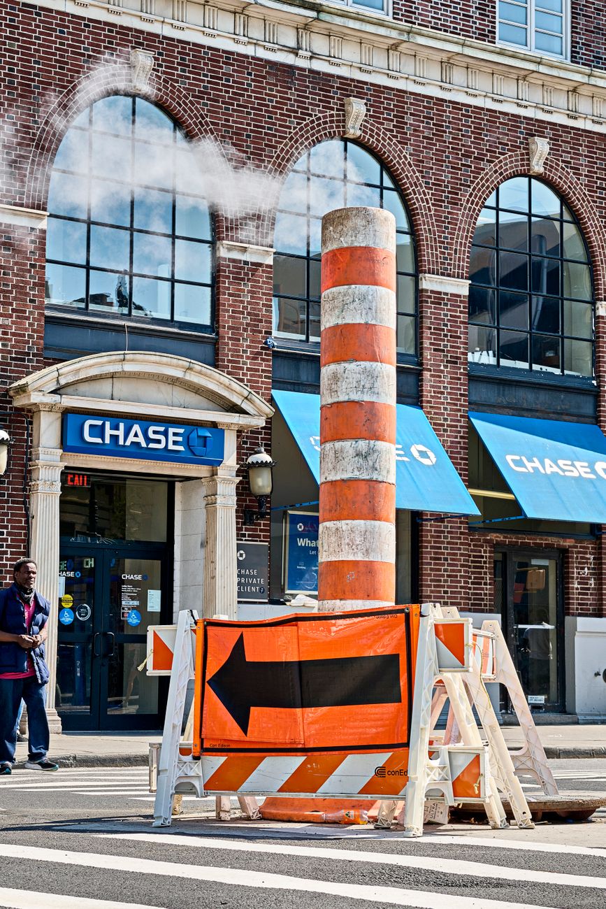 Steam rising on a New York street with a Chase Bank branch in the background.