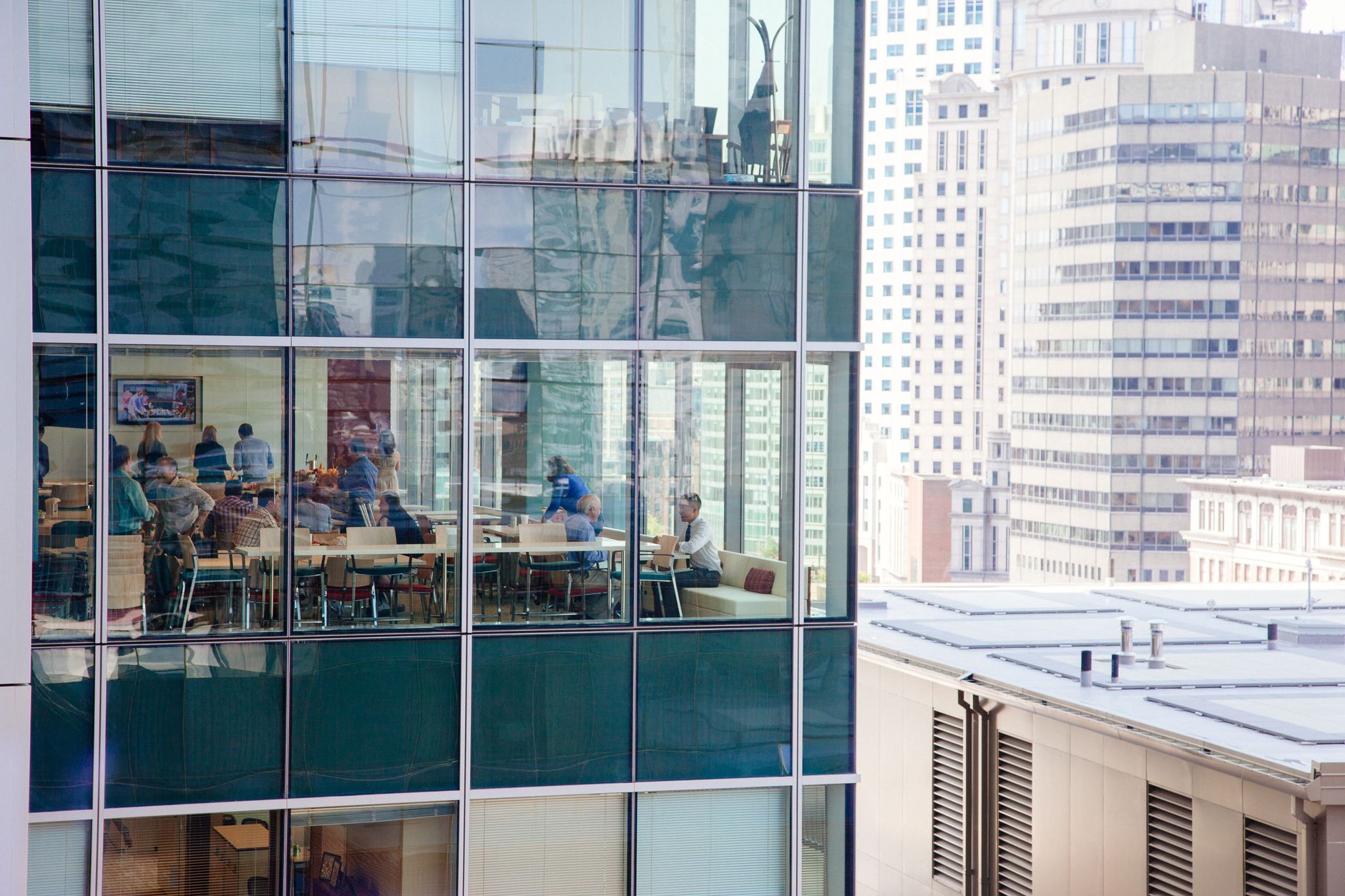 Urban office building with a glass facade reflecting New York City skyline and interior workspace activity.